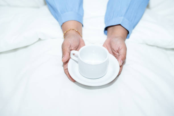 A woman holds a cup on the bed