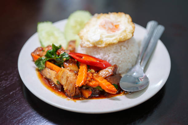 Stir-fried mixed vegetable pork belly served with fragrant white rice and a fried egg, a traditional Thai street food dish.
