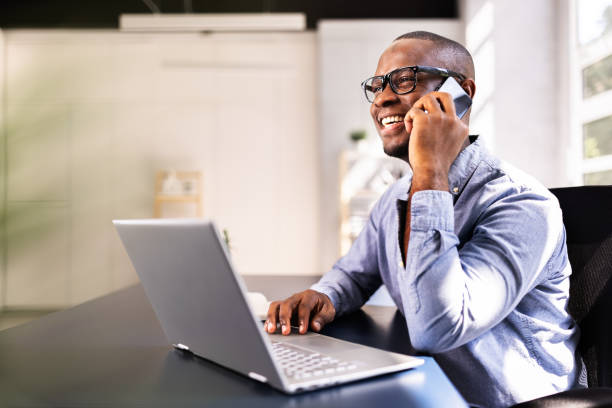 istock Smiling African-American businessman multitasking on smartphone at desk 2158807996