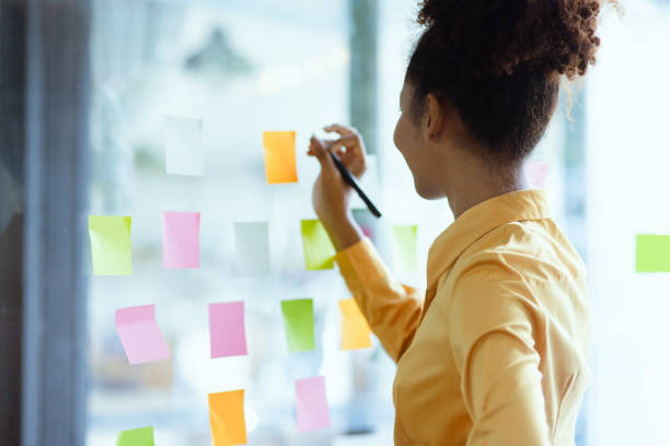 istock Young African American stylish woman working on project plan using sticky papers notes on glass wall. 2158809643