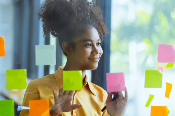 istock Young African American stylish woman working on project plan using sticky papers notes on glass wall. 2158809647