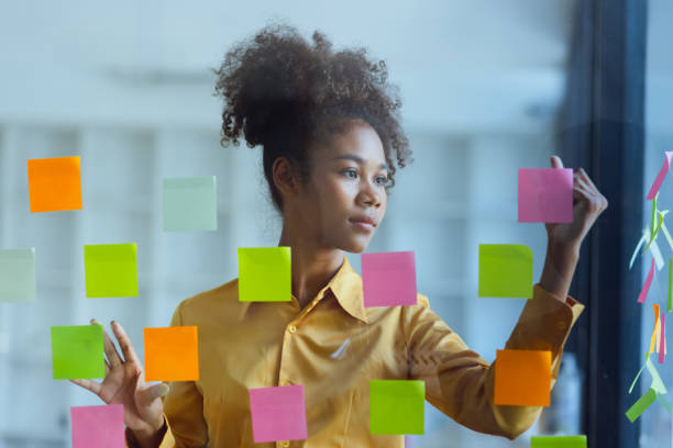 istock Young African American stylish woman working on project plan using sticky papers notes on glass wall. 2158809650
