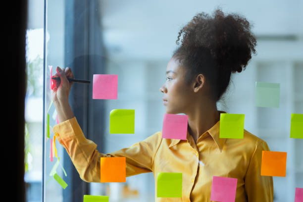 istock Young African American stylish woman working on project plan using sticky papers notes on glass wall. 2158809654