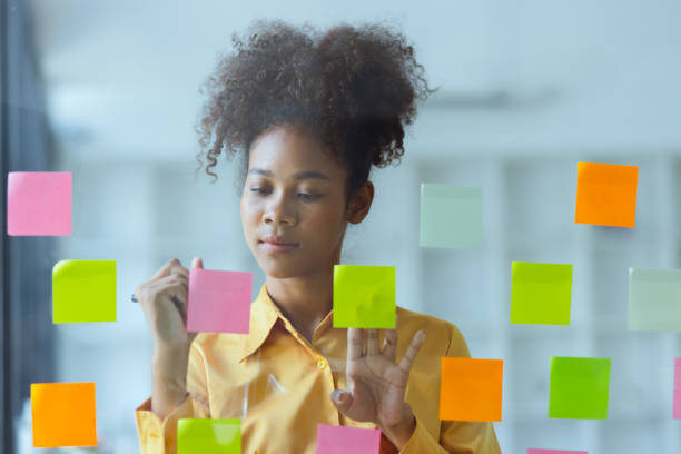 istock Young African American stylish woman working on project plan using sticky papers notes on glass wall. 2158809657