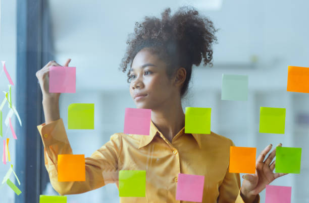 istock Young African American stylish woman working on project plan using sticky papers notes on glass wall. 2158809664
