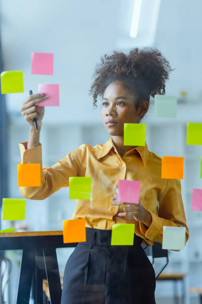 istock Young African American stylish woman working on project plan using sticky papers notes on glass wall. 2158809667