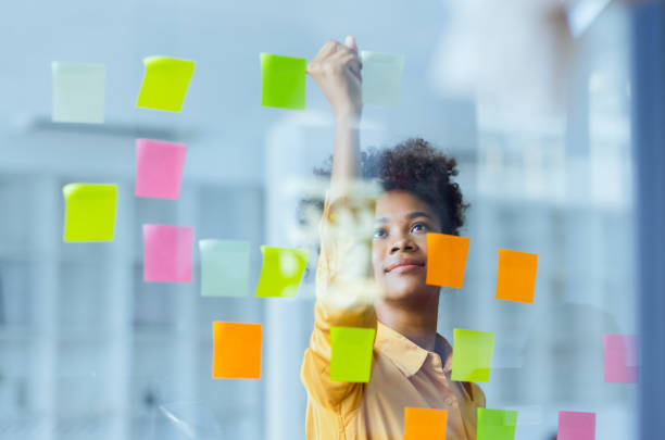 istock Young African American stylish woman working on project plan using sticky papers notes on glass wall. 2158809698