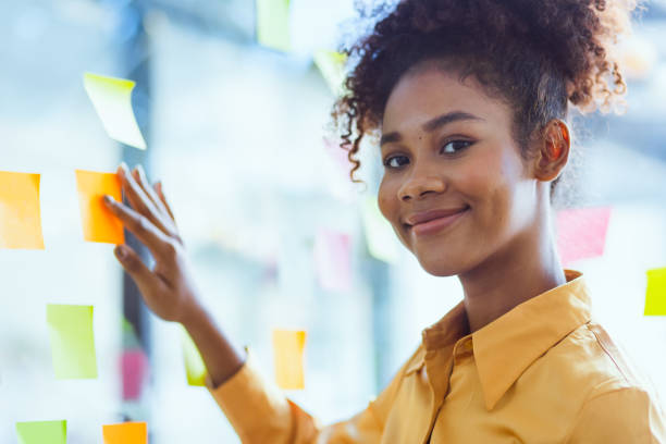 istock Young African American stylish woman working on project plan using sticky papers notes on glass wall. 2158809699