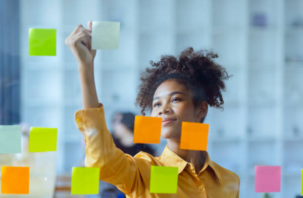istock Young African American stylish woman working on project plan using sticky papers notes on glass wall. 2158809704