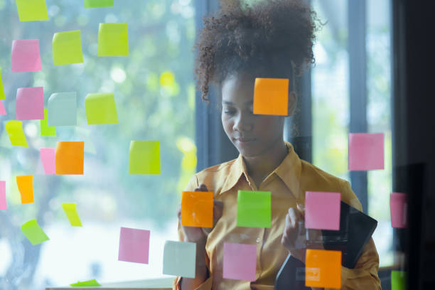 istock Young African American stylish woman working on project plan using sticky papers notes on glass wall. 2158809725