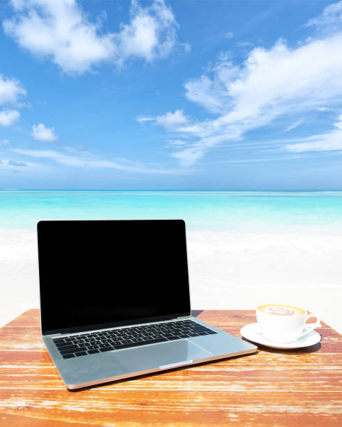 istock Laptop computer and coffee cup on the table at sunny beach 2158809973