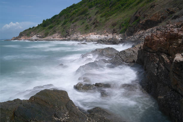 Waves crash against a rocky shoreline with mountains in the background