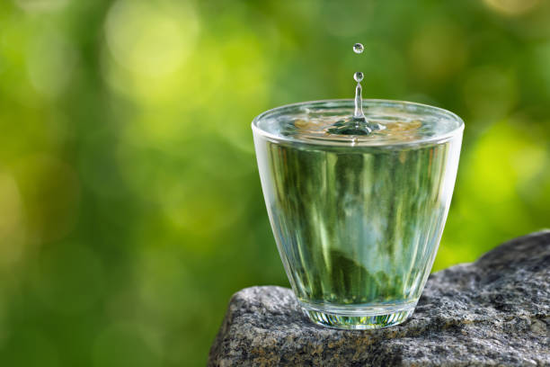 glass of drinking water with splash and drop on stone