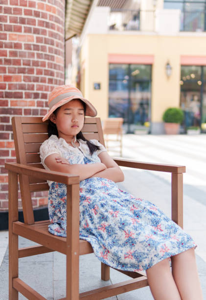 Summer hat hangs on the corner of a park bench, in the background you can see a wall and in the distance pink cherry blossom trees and a park landscape, 1:1