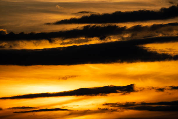The sun sets below the horizon, casting a warm glow of orange, pink, and purple across the sky. Silhouetted trees and hills frame the tranquil scene, capturing the breathtaking beauty of nature.