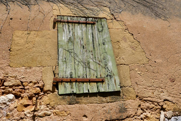Ancient shabby weatherworn shutter with rusty wrought iron hinges in a French medieval village