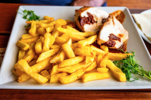 French fries with chicken roulade with dried tomato, sprouted pea leaf on white square plate.
