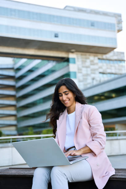istock Focused young middle eastern Israel businesswoman using laptop pc online application for work sitting outdoors. Indian or arabic woman manager in business suit working, typing on computer. Vertical 2158826931