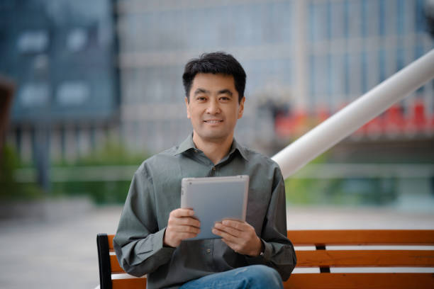 Middle-aged man using digital tablet while sitting on bench in city street