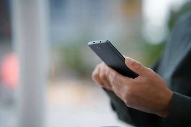 istock Middle-aged man using smartphone while sitting on bench in city street 2158827844