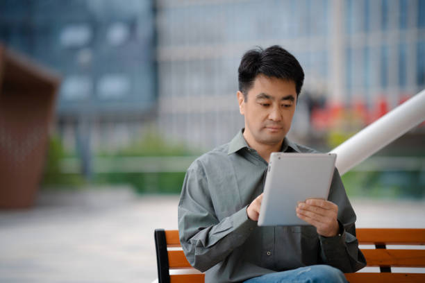 Middle-aged man using digital tablet while sitting on bench in city street