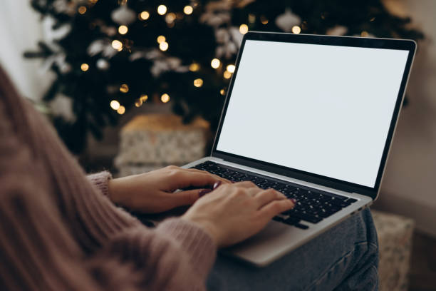 istock woman work on laptop computer with blank display screen with mockup copy space. home interior decorated for Christmas celebration with Christmas tree and garland lights. 2158836267