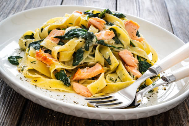 Pappardelle with grilled salmon and spinach on wooden table