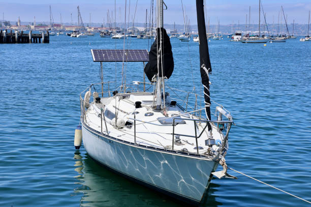 San Diego Bay, San Diego, CA, USA - October 1, 2014. As a sailboat boat tacks over the  waters of San Diego Bay, the city’s iconic skyline serves as a dramatic backdrop. The wind blows hard against the sail as the boat leans to the left. A man stands at the rear manning the sails. Behind the man are several passengers relaxing in the sun. Downtown San Diego’s towering skyscrapers rise majestically in the distance, and stand as a testament to San Diego's blend of natural beauty and urban sophistication. The scene is a perfect harmony of serene seascape and vibrant city life, capturing the essence of San Diego’s unique charm.
