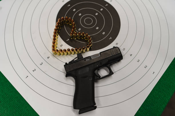 istock Shooting from a pistol at a shooting range. A paper target for shooting, a pistol and 9mm cartridges are laid out in the shape of a heart. 2158844570