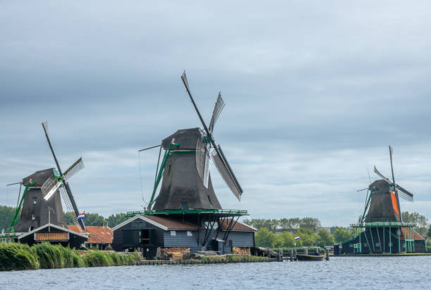 The Netherlands. A cloudy summer day in Zaanse Schans. Three old but functioning windmills on the bank of a canal