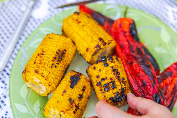 Close-up view of a hand taking grilled corn from a plate.