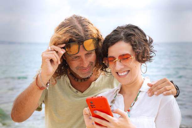 istock Smiling couple on the beach browsing smartphone apps. 2158853244