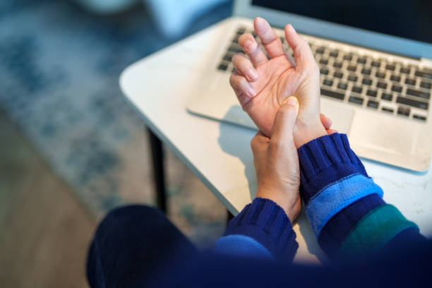 Cropped image of an Asian woman massaging her arthritic hand and wrist after long hours in front of a computer, indicating pain and rheumatism. stock photo
