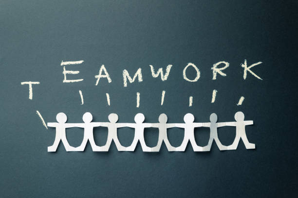 Teamwork concept, with paper humans holding hands together, with text by chalk, and each different alphabet represents each doll
