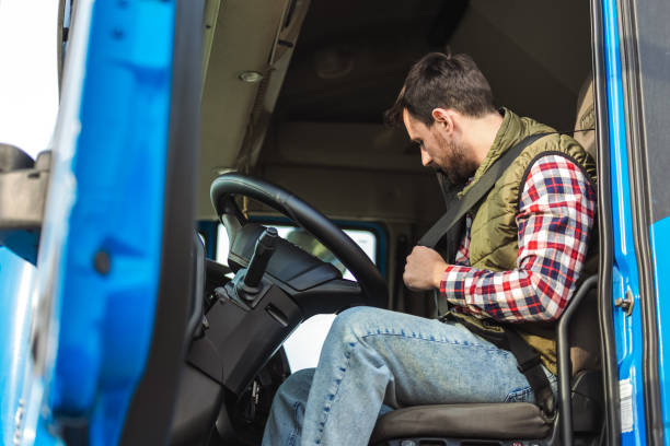 Young truck driver putting safety belt on, in his truck. stock photo