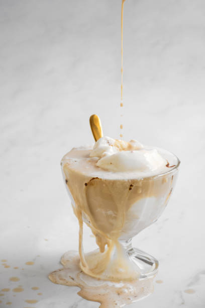 istock melting ice cream in a glass cup with a spoon, topped with dripping sauce on a white background. 2158858721