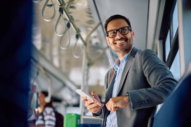 Happy businessman using cell phone and listening music while commuting by bus.