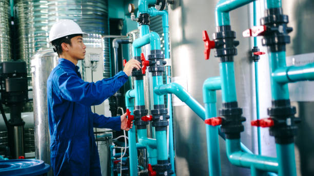 istock Maintenance engineer Worker in a hard hat adjusting valves and examining  pressure gauge on industrial piping in a water treatment facility. water bottling 2158874009