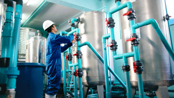 istock Maintenance engineer Worker in a hard hat adjusting valves and examining  pressure gauge on industrial piping in a water treatment facility. water bottling 2158874011