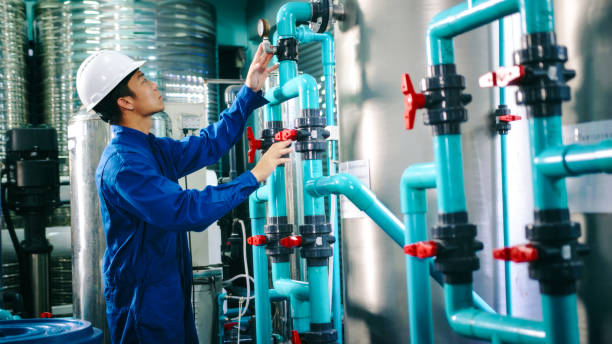 istock Maintenance engineer Worker in a hard hat adjusting valves and examining  pressure gauge on industrial piping in a water treatment facility. water bottling 2158874012