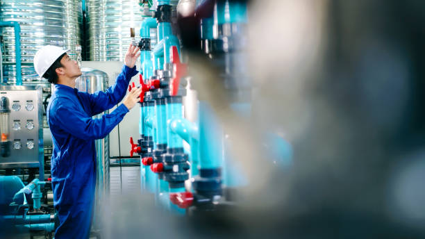 Maintenance engineer Worker in a hard hat adjusting valves and examining  pressure gauge on industrial piping in a water treatment facility. water bottling