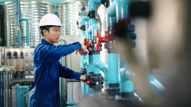 istock Maintenance engineer Worker in a hard hat adjusting valves and examining  pressure gauge on industrial piping in a water treatment facility. water bottling 2158874020