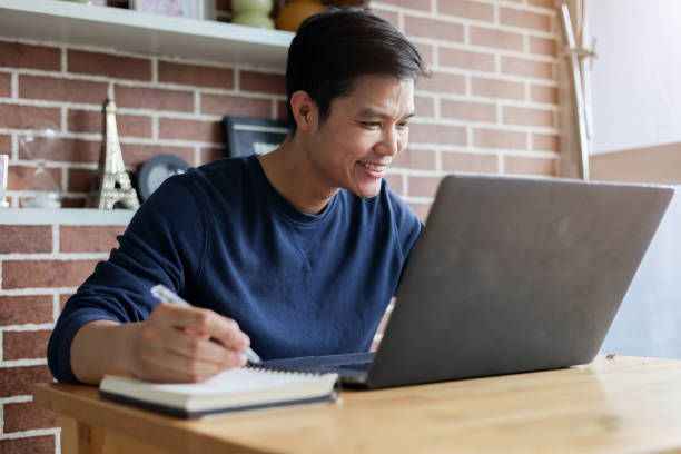 istock close up young asian student man sitting at the library in university and learning online course and doing assignment by writing on notebook for education and lifestyle concept 2158874780