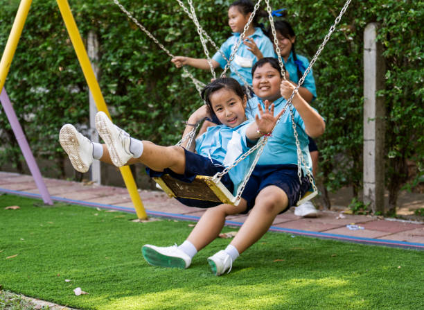 School children in uniforms enjoying the swings on the playground during recess