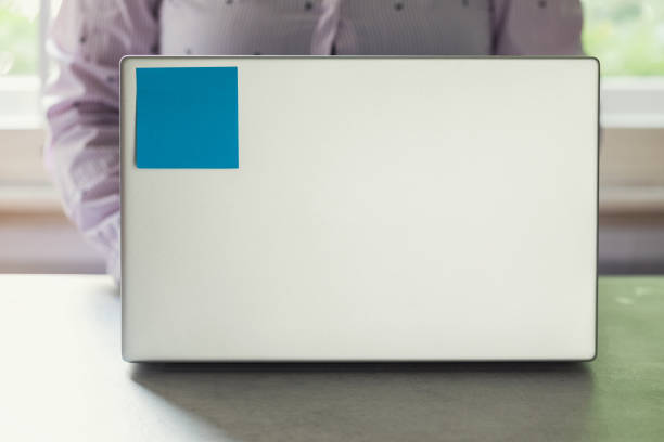 Close-up of blue sticky notes on a laptop cover with person working in the office