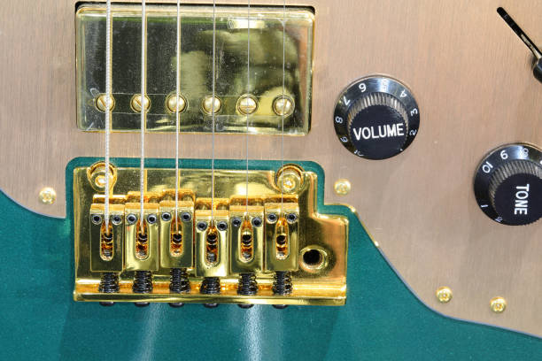 Close-up of electric guitar bridge with volume and tone knobs and gold pickup