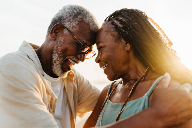 Senior African American couple embracing on the beach at sunset Loving senior African American couple sharing an intimate moment with their foreheads touching on a sunny beach. black couple sunset stock pictures, royalty-free photos & images
