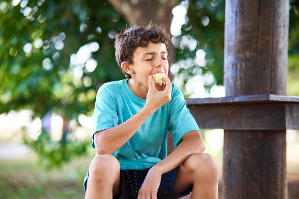 Portrait of a young boy eating a fruit in a park.