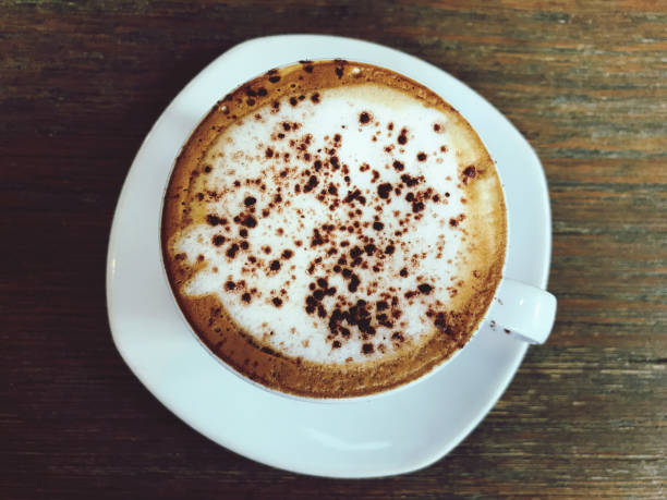 Cappuccino coffee in white cup on wooden table, top view