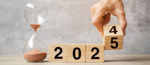 hand flipping block 2024 to 2025 text with hourglass on table. Resolution, time, plan, goal, motivation, reboot, countdown  and New Year holiday concepts